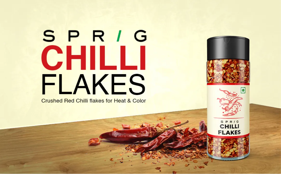 A jar of crushed red chilli flakes on a wooden table with dried chillies