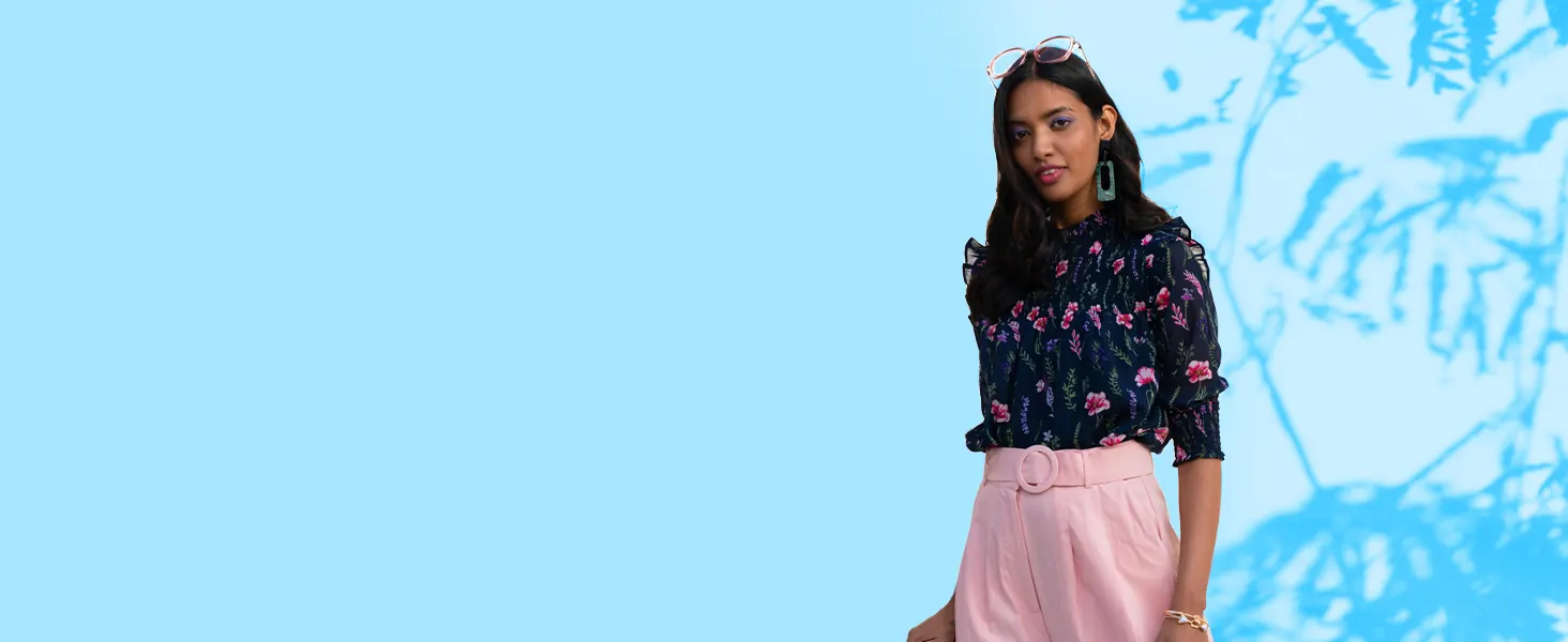 A woman in a navy floral top and pink trousers against a blue wall
