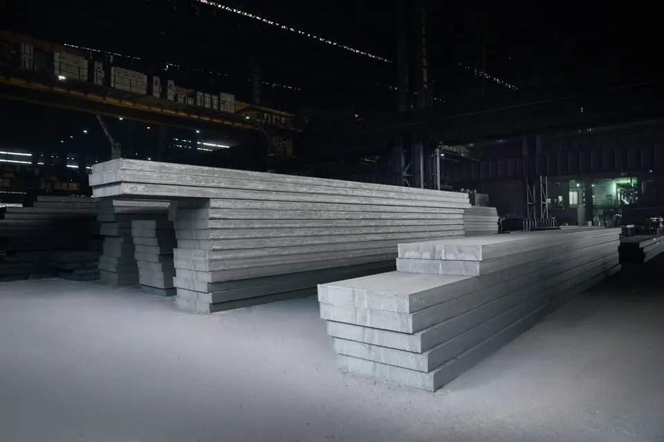 Long steel slabs stacked in a dim factory bay
