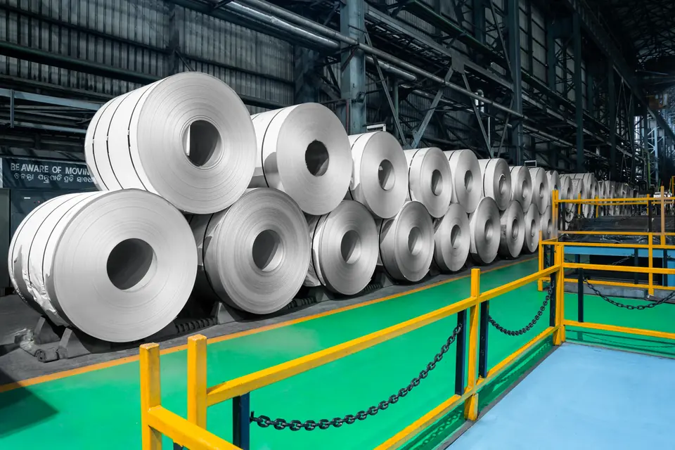 Bright steel coils stacked two high behind a yellow railing