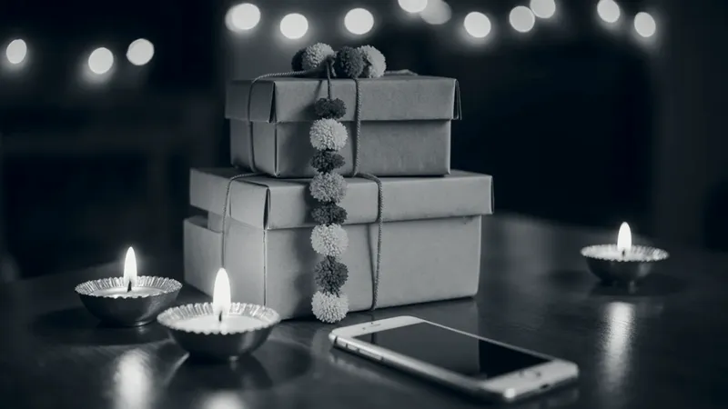 Delivery parcels tied with a marigold garland beside lit diyas and a phone, on a table in the evening