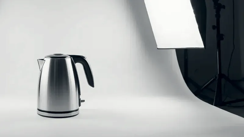A steel electric kettle on a white paper backdrop, lit by a softbox on a stand