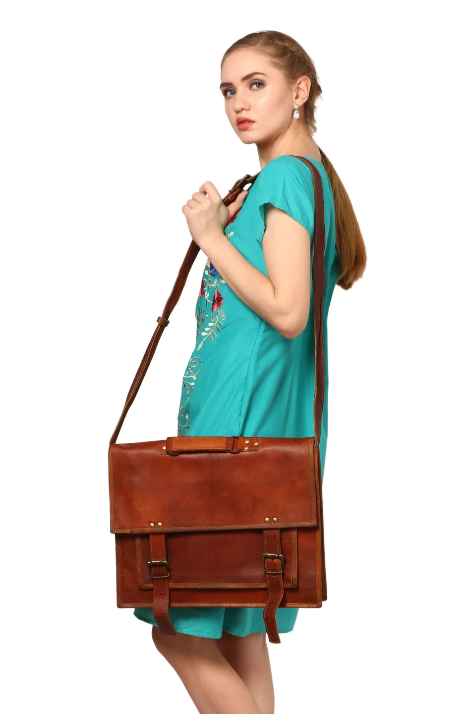 A model in a turquoise dress with a brown leather satchel on her shoulder, on white