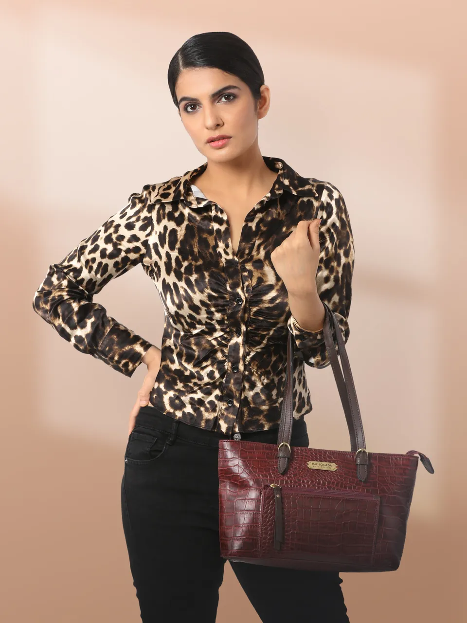 A model in a leopard-print shirt holding a burgundy croc-textured tote, against a peach wall