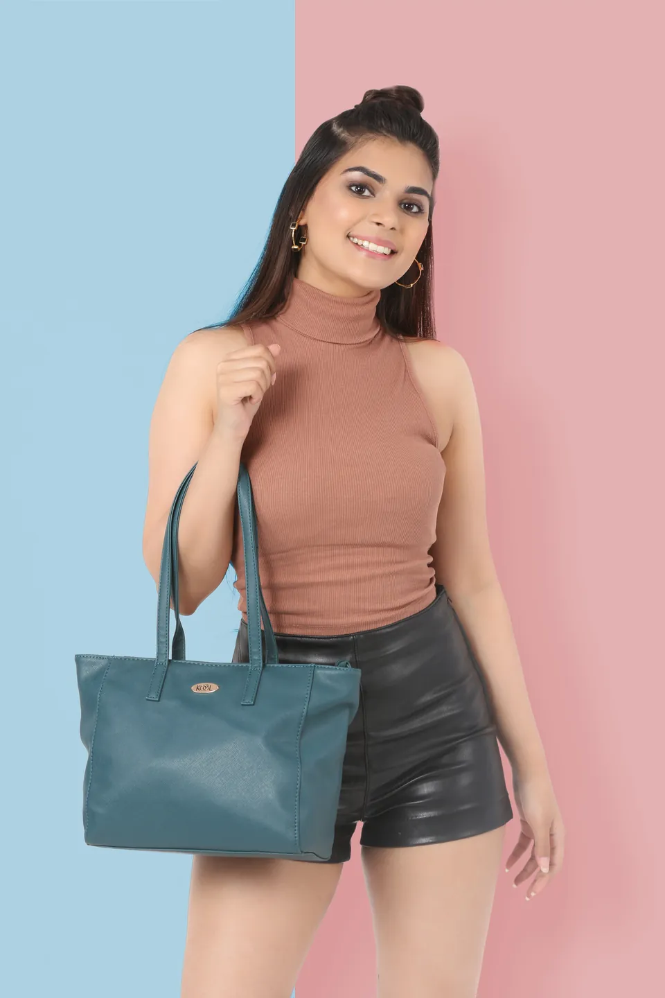 A smiling model in a tan sleeveless top with a teal tote on her shoulder, against a blue and pink wall