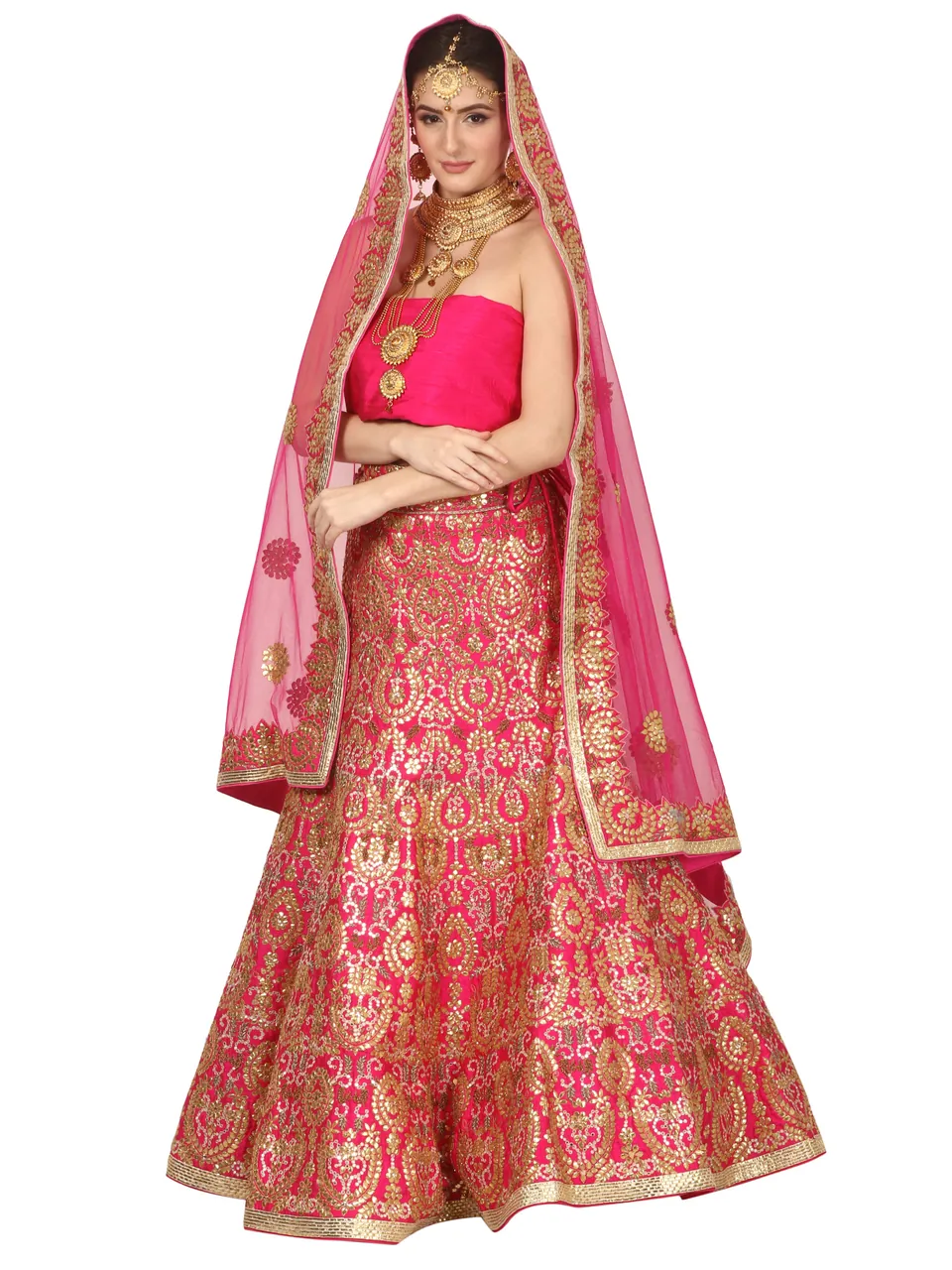 A model in a pink bridal lehenga with gold embroidery, a sheer pink dupatta over her head, on white