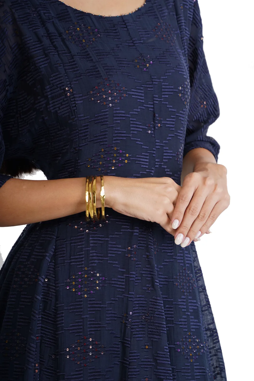 Gold bangles on a model’s wrist, her hands folded over a navy dress