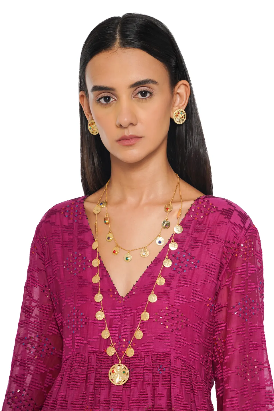 A model wearing a layered gold coin necklace and earrings over a magenta top