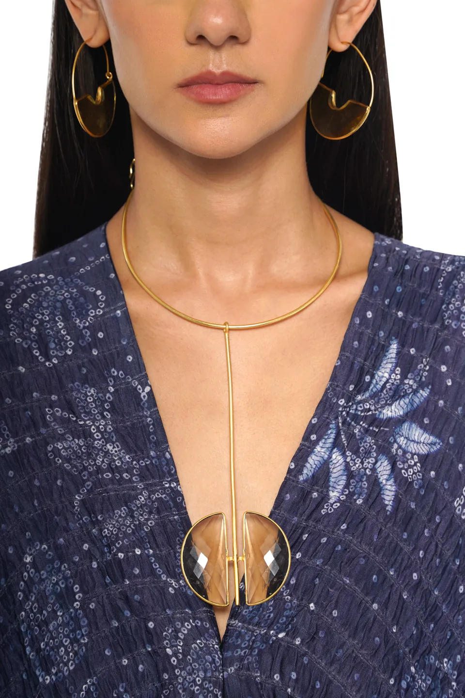 A gold collar necklace with a clear crescent pendant, worn over a navy dress