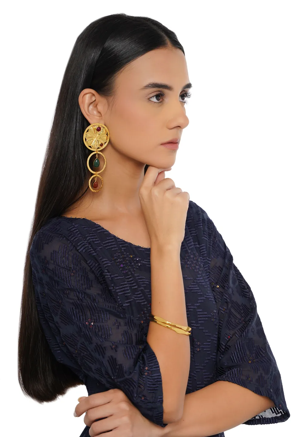 A model in profile wearing a long gold statement earring and a gold cuff