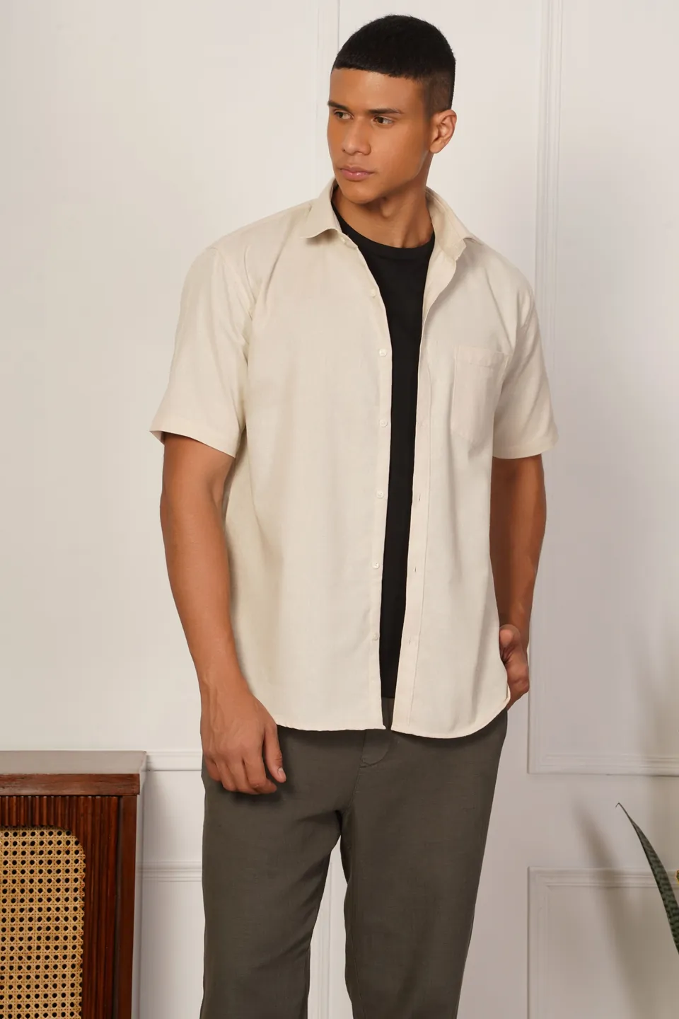 A male model in a cream short-sleeved shirt over a black T-shirt, in a styled room