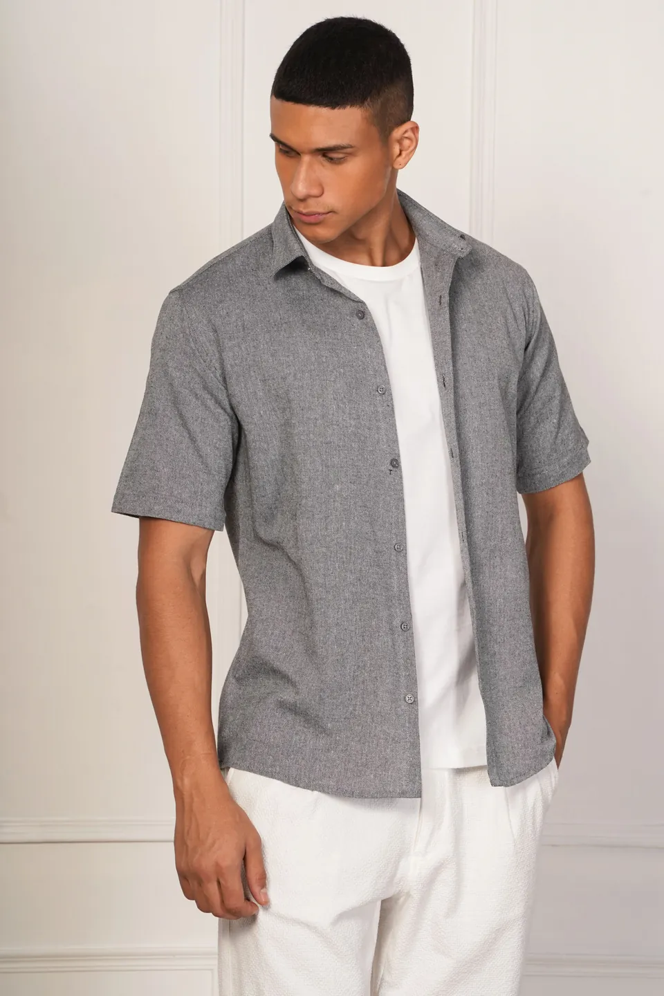 A male model in a grey shirt over a white T-shirt, in a styled room