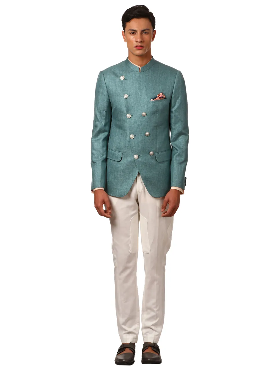 A male model in a teal double-breasted bandhgala jacket and white trousers, on white
