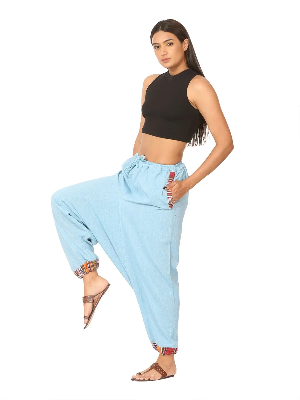 A model in a black crop top and sky-blue harem pants, one knee raised, on white