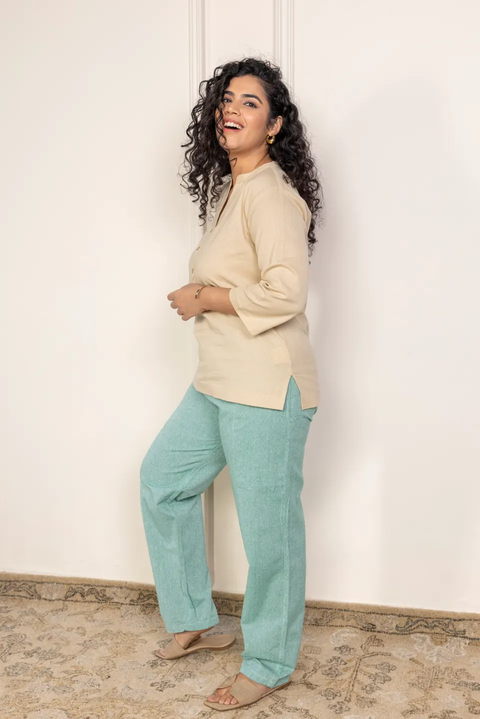 A female model in a beige linen top and mint trousers, smiling